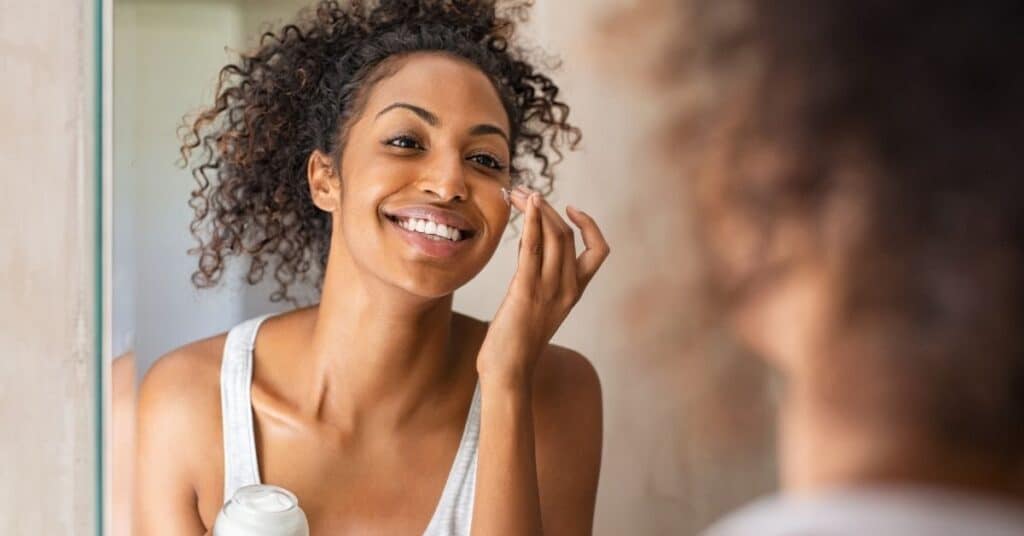 A woman looks in the mirror and applies face lotion | Chronic skin conditions