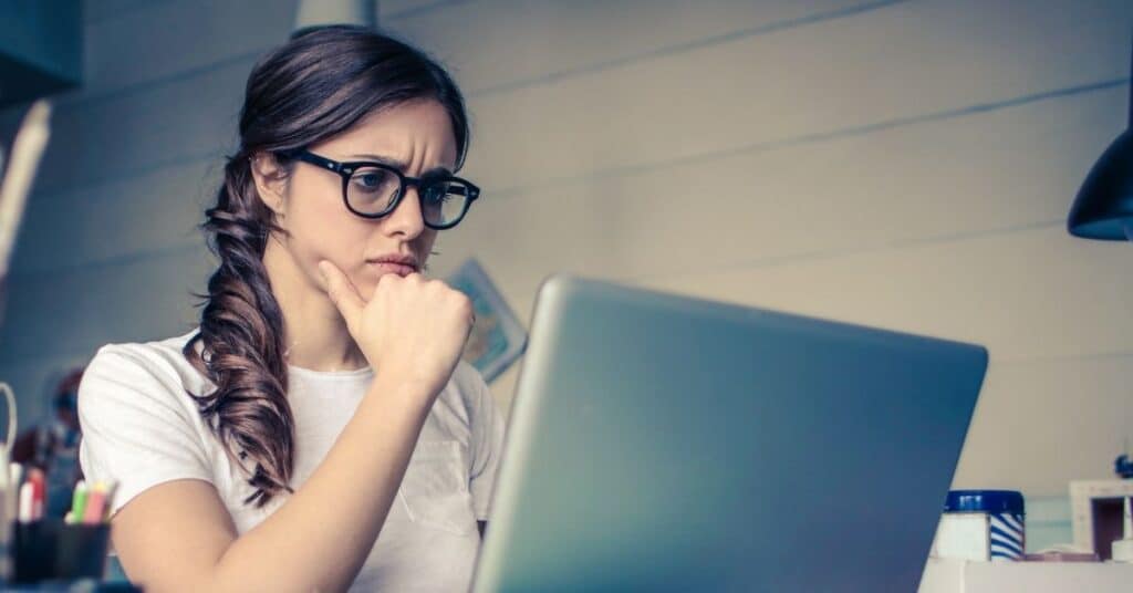 A woman with a stressed look on her face looks at a laptop presumably researching her digestive issue symptoms
