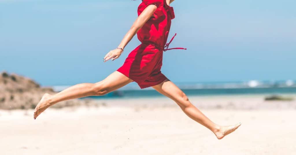 Woman in jumper leaping across a sandy beach in joy