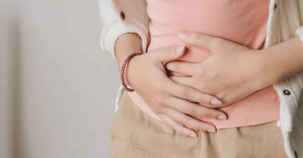 Woman holds her gut in her hands, as if she is nauseous our bloated