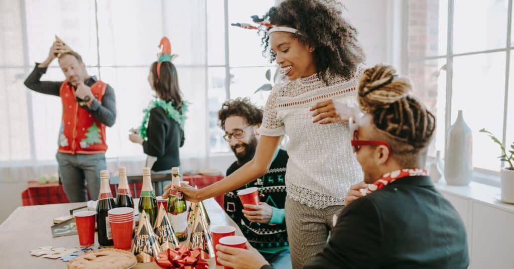 A woman at a holiday office party lifts a bottle of champagne off a table, staying healthy during the holidays