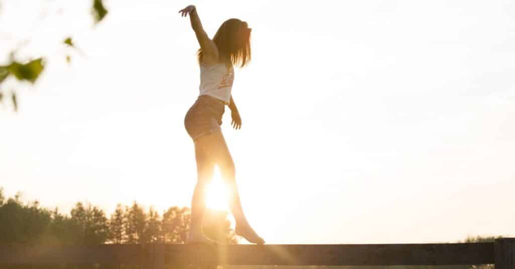 A young woman balances on a beam with the sun shining behind her