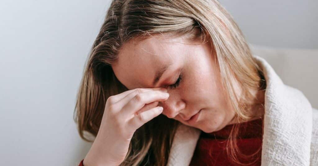 A woman pinches at her brow with her head down and eyes closed, IBS symptoms in females