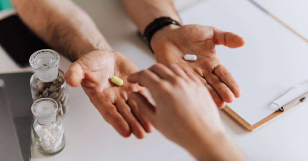 A doctor holds out both hands, each one with a different pill in it, someone else's hand reaches out to pick one