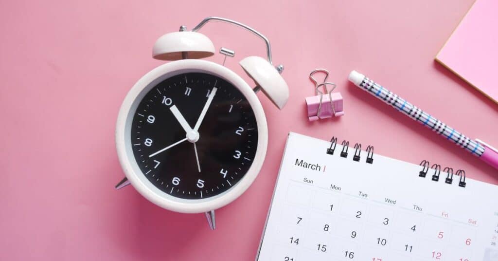 A traditional alarm clock is sitting on a table next to a calendar and paper clip