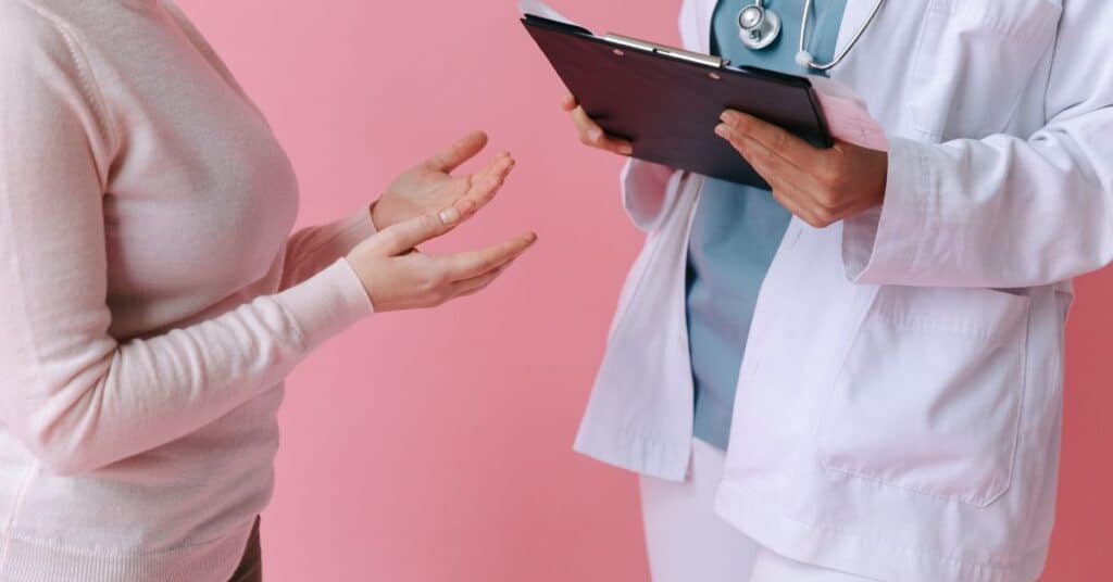 A woman's torso and hands are in action showing that she is talking, while a doctor holds up a clipboard, Problems with doctor patient communication