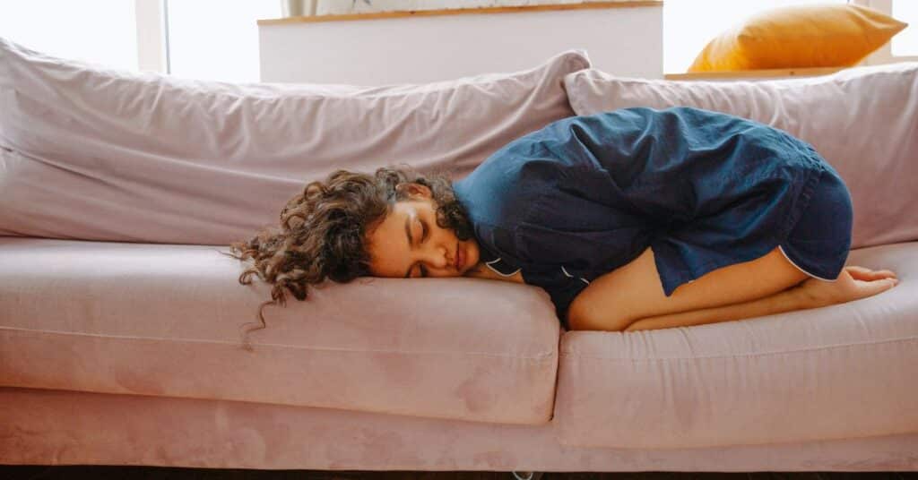 Woman curled in a ball on her couch with menstrual cramps, hormones and gut health