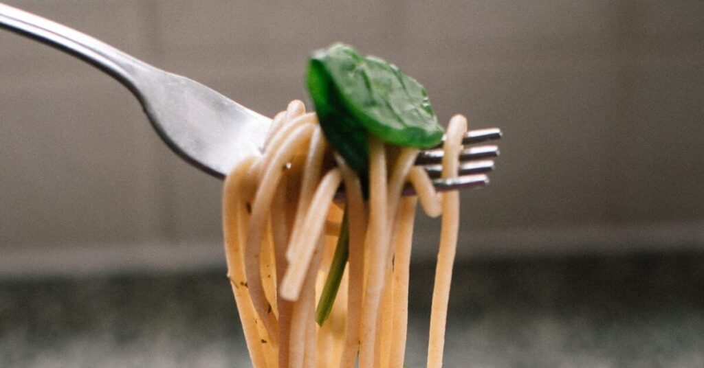 A lifted fork with a bite of pasta and spinach on it