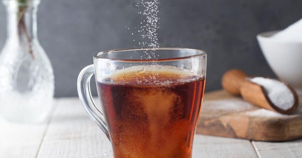 Sugar granules fall into a hot cup of tea