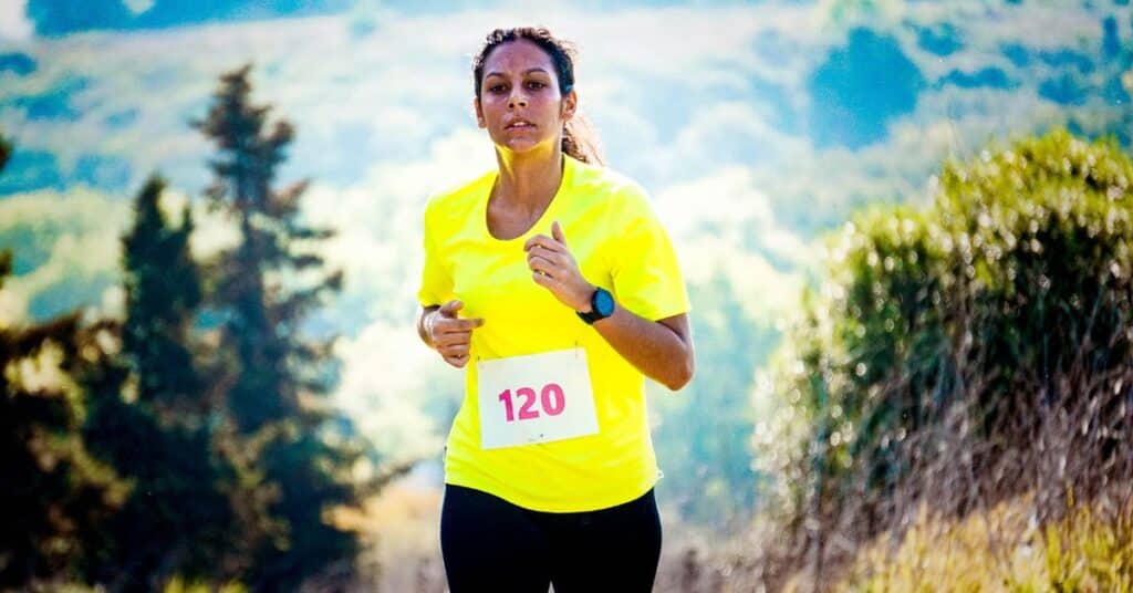 A woman in a bright t-shirt with a number tag pinned to it runs in a race, story of reducing IBS symptoms