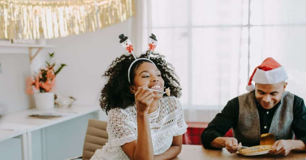 A woman wearing a festive headband takes a bite of dessert at a holiday office party, IBS flare up