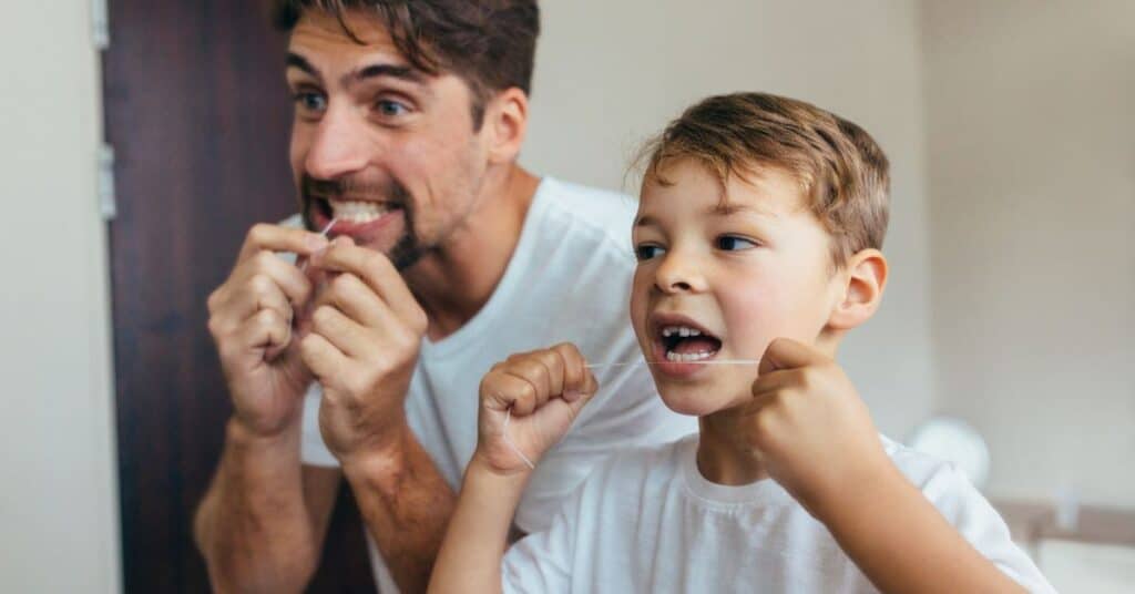 A father and son both floss their teeth together, how oral health affects overall health