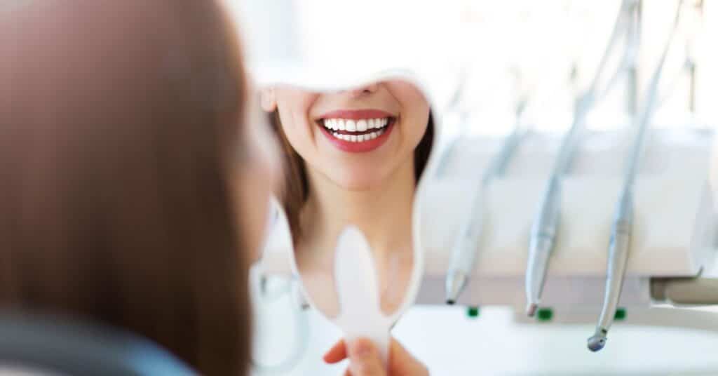 A woman smiles wide with a clean, bright smile in a dentist's mirror, how oral health affects overall health