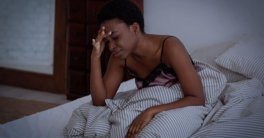 A women sits up in bed with her hand resting on her forehead as if she has a headache