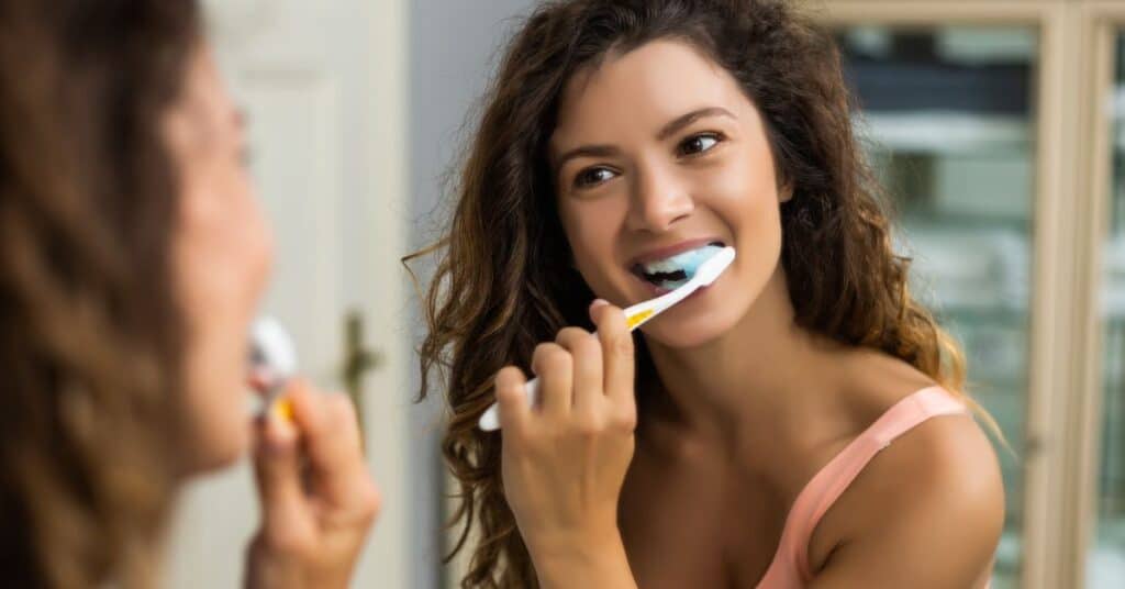 A young woman brushes her teeth, how oral health affects overall health