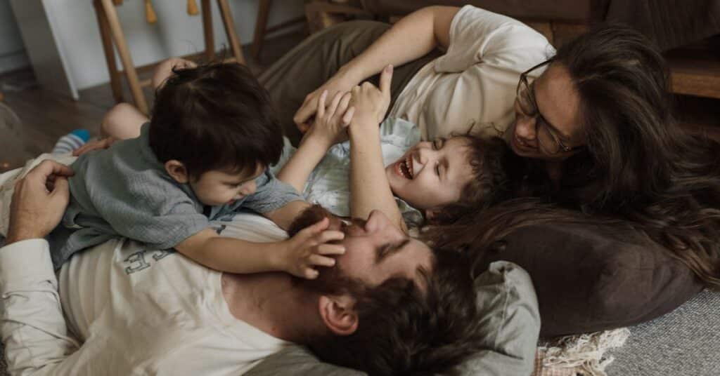 A family of four laughs and plays on the living room floor together