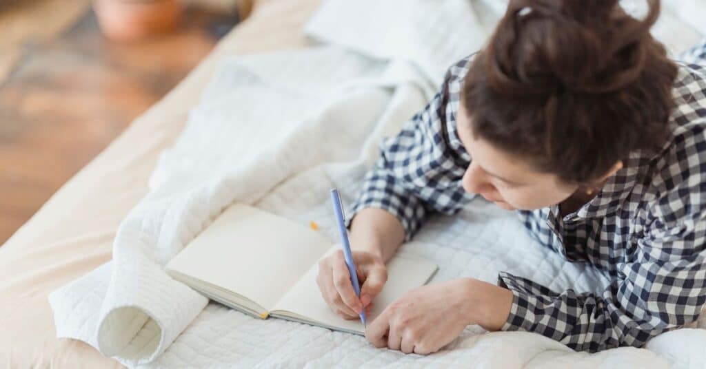 Busy woman lays in a bed and writes in her journal