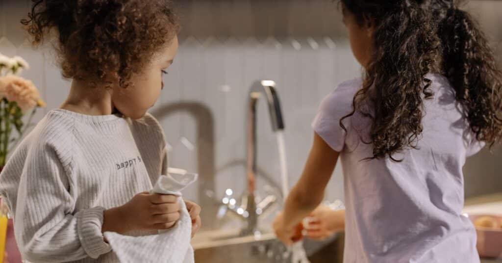 Two young kids do the dishes together, hot mess mom culture